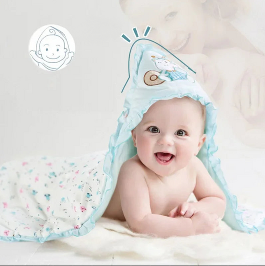 Bébé souriant allongé sous une couverture d’emmaillotage en coton bleu avec capuche brodée, douce et chaude, idéale pour nouveau-né en hiver