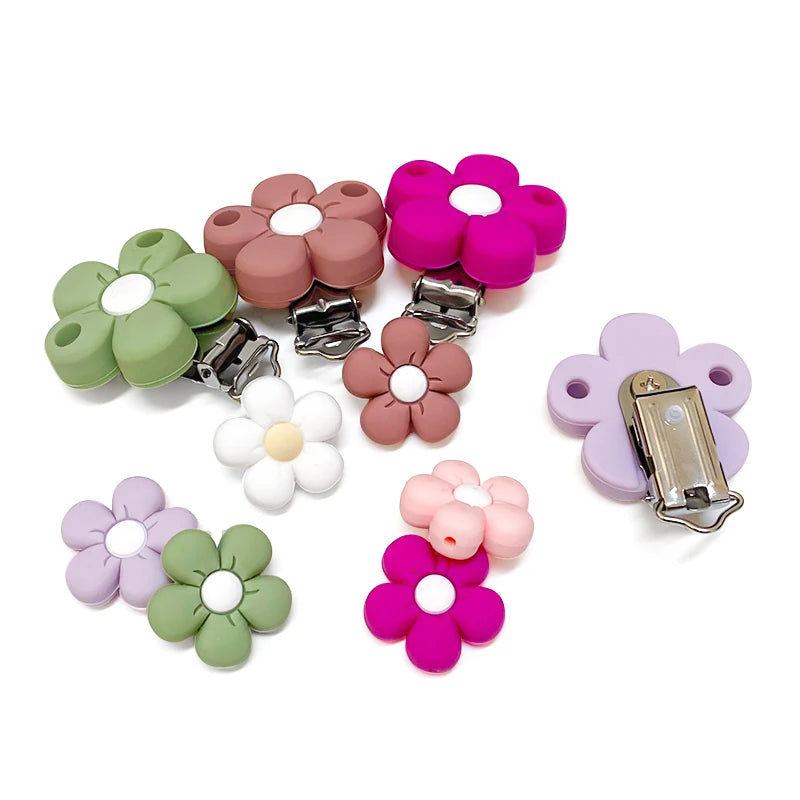 Assortiment de clips attache-tétine et perles en silicone en forme de fleur, coloris pastel (vert sauge, terracotta, fuchsia, lilas, blanc et rose), avec vue du mécanisme métal au dos.