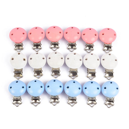 Alignement de clips attache-tétine en bois peint rose, blanc et bleu, avec trous de ventilation et pinces métalliques, présentés sur fond blanc.