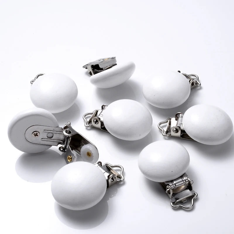 Ensemble de clips attache-tétine en bois peint blanc, de forme lisse et arrondie, équipés de pinces métalliques, disposés sur fond blanc.