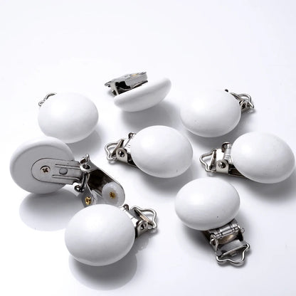 Ensemble de clips attache-tétine en bois peint blanc, de forme lisse et arrondie, équipés de pinces métalliques, disposés sur fond blanc.