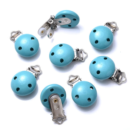Ensemble de clips attache-tétine en bois peint bleu canard, avec trous de ventilation et pinces métalliques, disposés sur fond blanc.