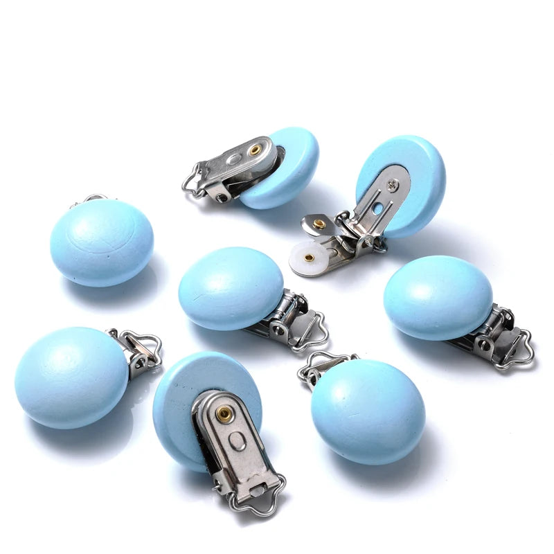 Ensemble de clips attache-tétine en bois peint bleu clair, de forme lisse et arrondie, équipés de pinces métalliques, disposés sur fond blanc.