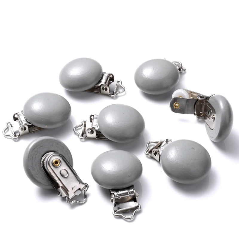 Ensemble de clips attache-tétine en bois peint gris, de forme lisse et arrondie, équipés de pinces métalliques, disposés sur fond blanc.