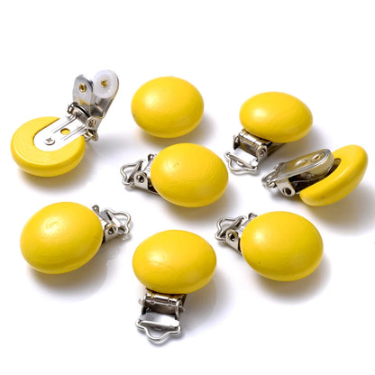 Ensemble de clips attache-tétine en bois peint jaune, de forme lisse et arrondie, équipés de pinces métalliques, disposés sur fond blanc.
