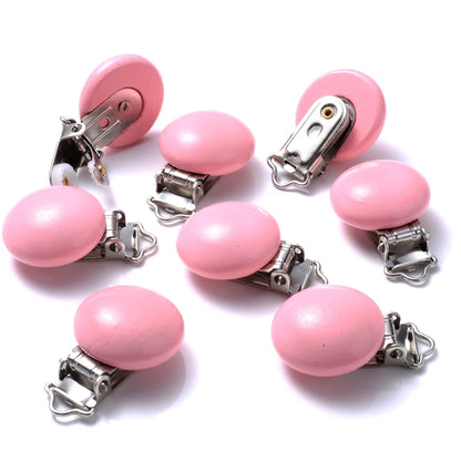 Ensemble de clips attache-tétine en bois peint rose, de forme lisse et arrondie, équipés de pinces métalliques, disposés sur fond blanc.