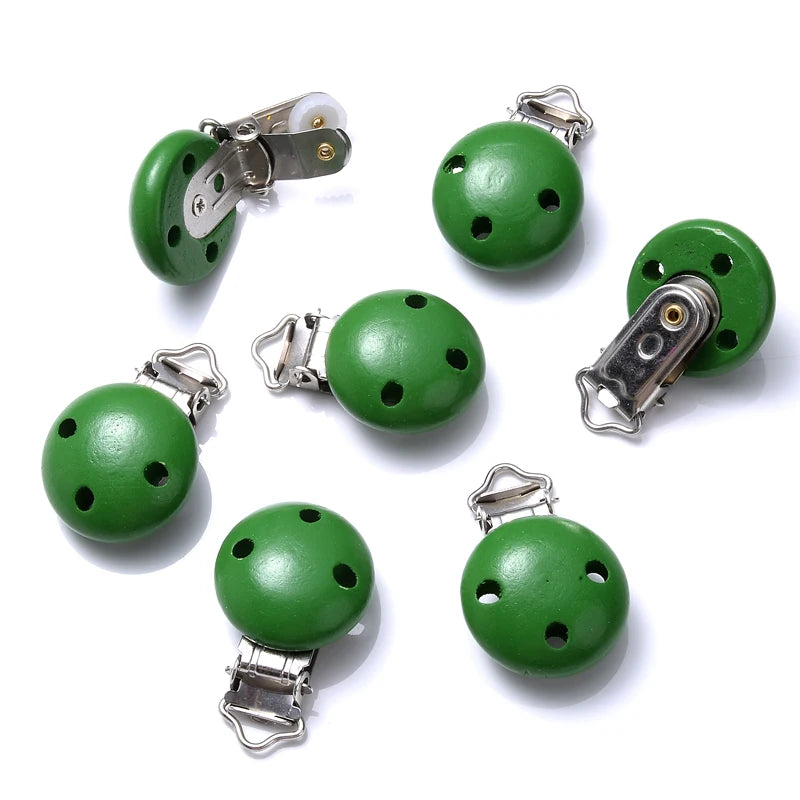 Ensemble de clips attache-tétine en bois peint vert, avec trous de ventilation et pinces métalliques, disposés sur fond blanc.