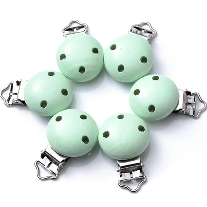 Ensemble de clips attache-tétine en bois peint vert menthe, avec trous de ventilation et pinces métalliques, disposés sur fond blanc.