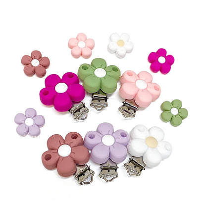 Assortiment de clips attache-tétine et perles en silicone en forme de fleur, coloris pastel (rose, vert sauge, lilas, blanc, fuchsia et terracotta), présentés en collection.
