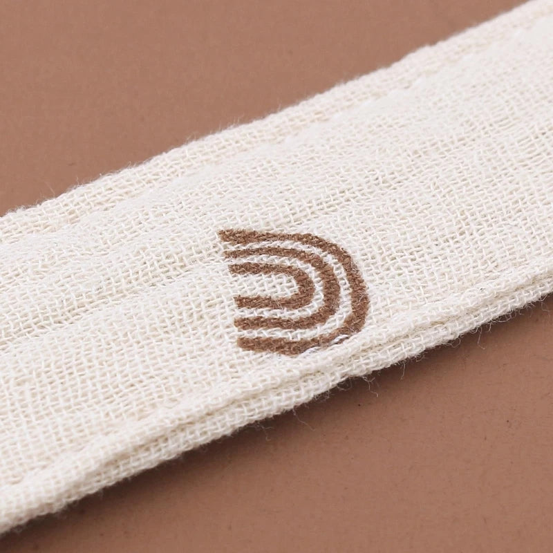 Gros plan sur le tissu en coton d’une attache-tétine avec logo imprimé, dans des tons naturels et doux.