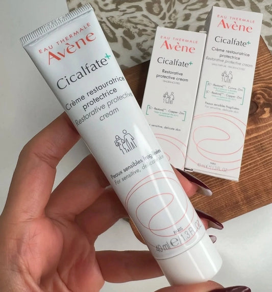 Main tenant un tube de crème réparatrice Avène Cicalfate+ 40ml avec boîtes en arrière-plan