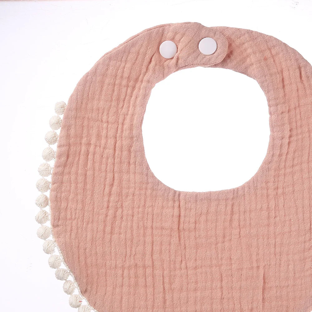 Détail d’un bavoir bébé en coton mousseline rose poudré avec bordure pompons et boutons-pression