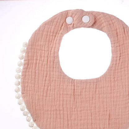 Détail d’un bavoir bébé en coton mousseline rose poudré avec bordure pompons et boutons-pression