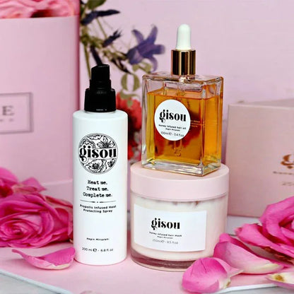 Coffret de soins Gisou comprenant le spray protecteur de chaleur, l’huile capillaire au miel et le masque nourrissant, présentés avec des fleurs roses