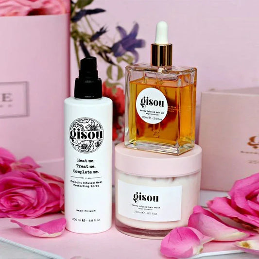 Coffret de soins Gisou comprenant le spray protecteur de chaleur, l’huile capillaire au miel et le masque nourrissant, présentés avec des fleurs roses