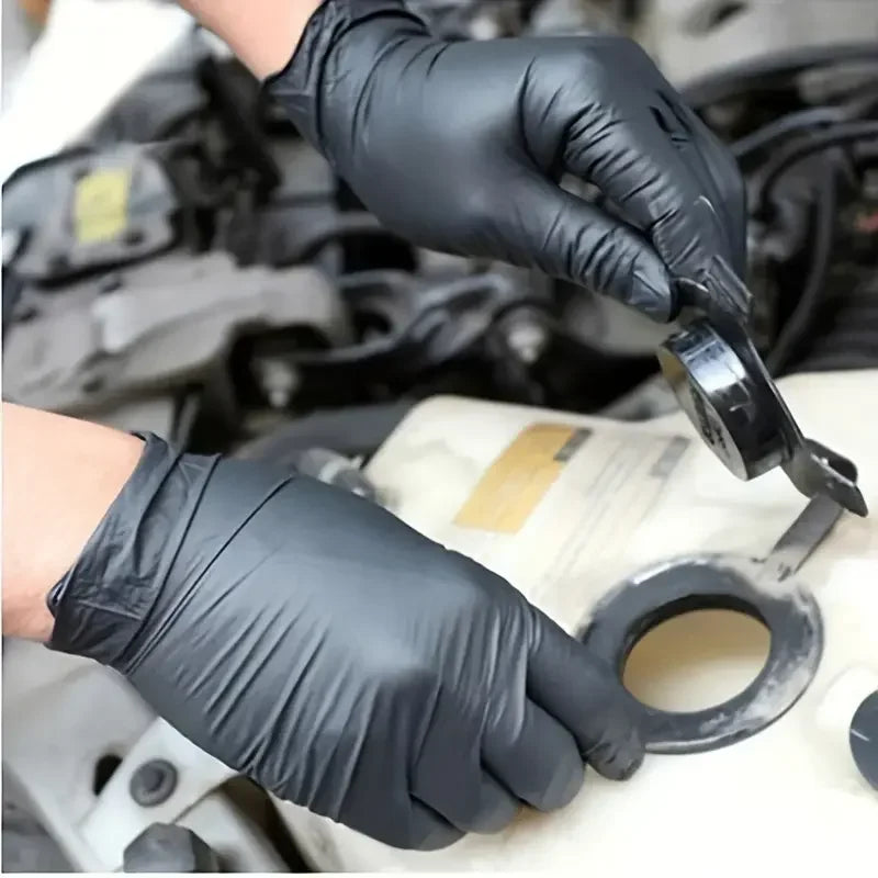 Mains portant des gants jetables en nitrile noir lors d’une intervention mécanique automobile, offrant protection, résistance et excellente adhérence en milieu gras.