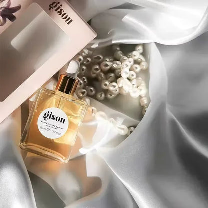Flacon d’huile capillaire Gisou au miel, format 20 ml, posé sur un tissu satiné avec des perles pour une mise en scène luxueuse