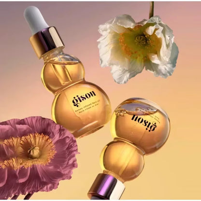 Bouteilles d’huile visage Gisou infusée au miel, mises en scène avec des fleurs colorées sur un fond dégradé