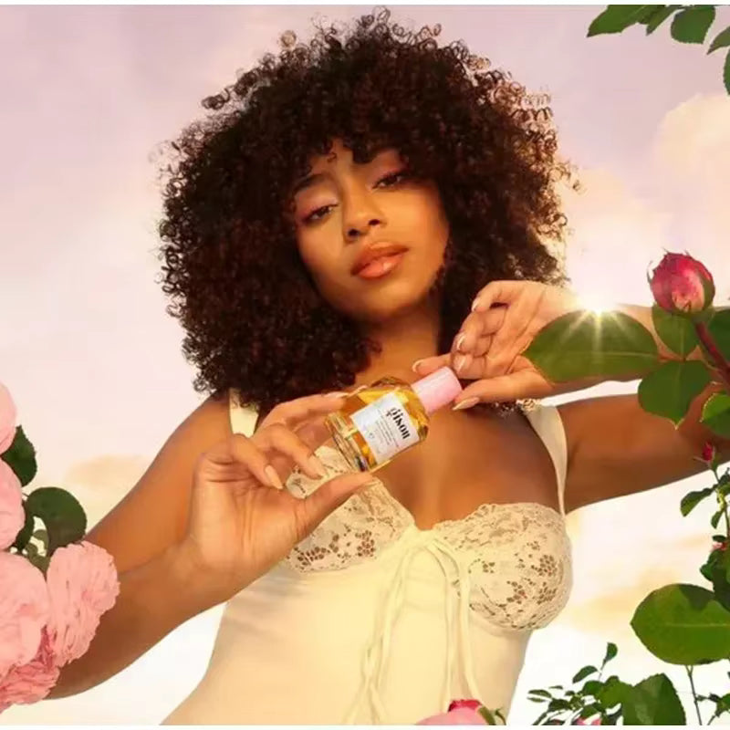 Modèle tenant le parfum pour cheveux Gisou au miel dans un décor floral lumineux au coucher du soleil