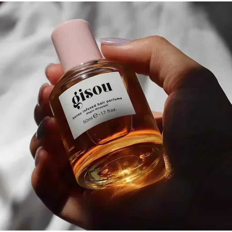Flacon de parfum pour cheveux Gisou au miel, format 50 ml, tenu en main sous une lumière naturelle